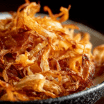 Homemade golden fried onions in a rustic bowl on a wooden table.