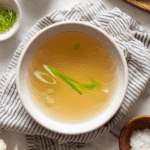Clear Thai style broth served warm with fresh herbs in a ceramic bowl.