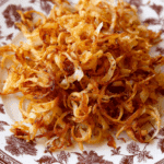 Homemade golden fried onions in a rustic bowl on a wooden table.